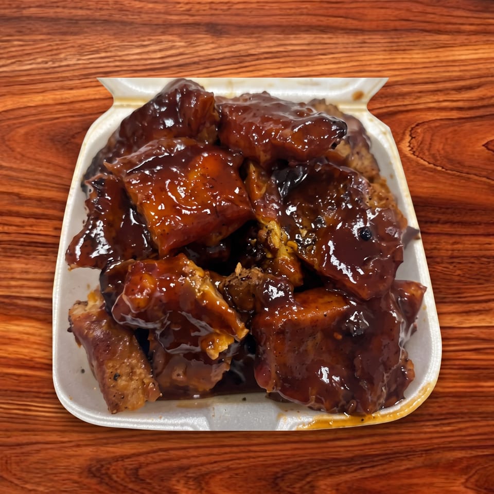 A white takeout container filled with glistening, dark brown barbecue chicken pieces on a wooden table.